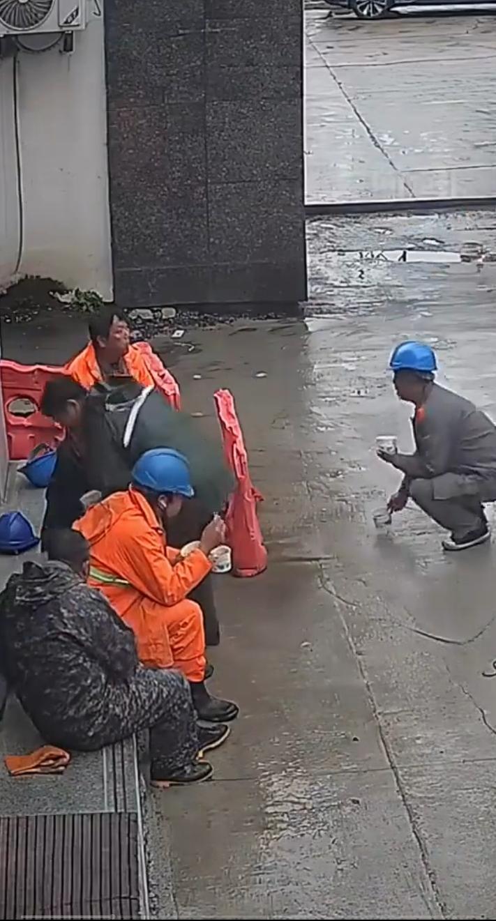警民一家亲，湖北黄石一群修路的工人正在吃午饭，不巧天空下起了蒙蒙细雨，工友们无意