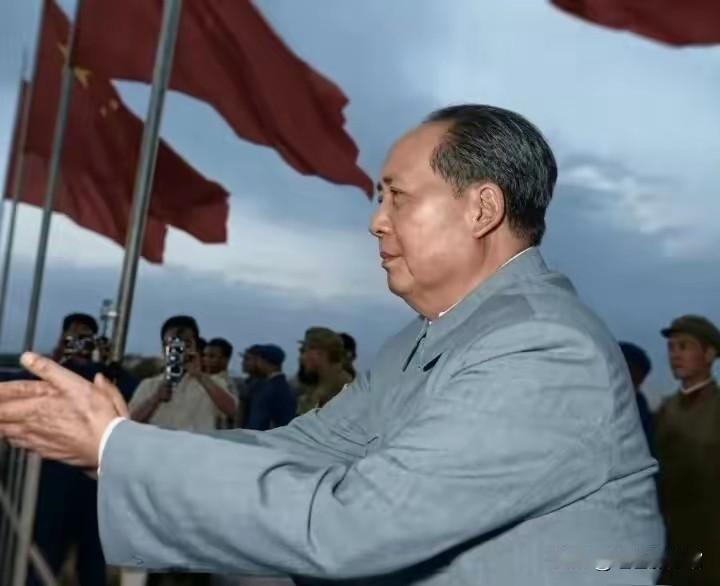 这是经彩色修复的经典历史影像，毛主席身着浅灰中山装抬手致意，身旁五星红旗迎风舒展
