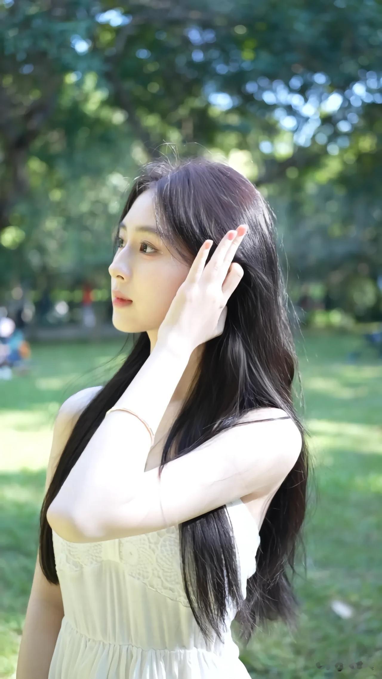 阳光洒落，温柔少女在绿意盎然的公园里轻抚发丝，静享美好时光。