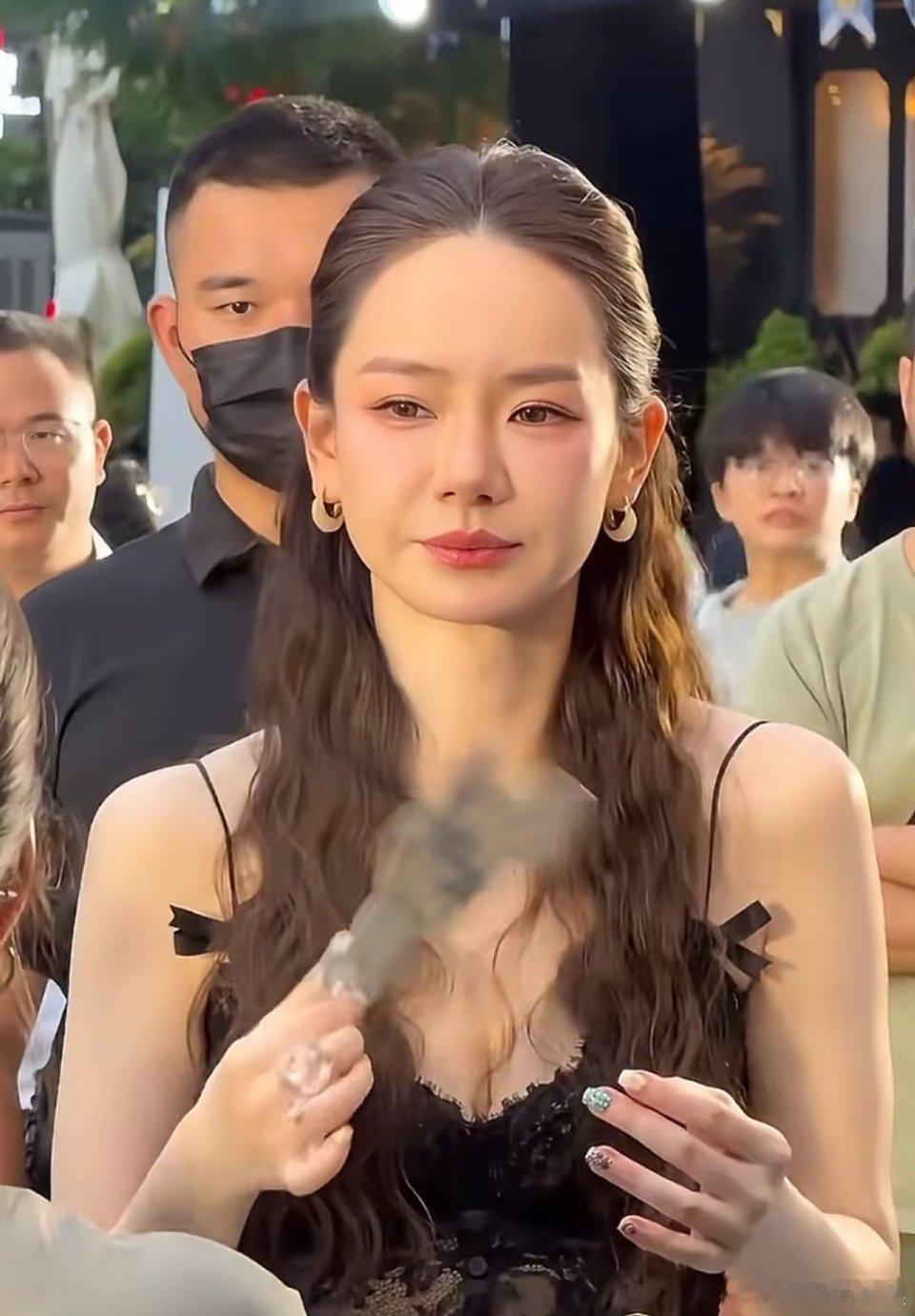 戚薇现身路人中间，她梳着弯曲的长发，身穿黑色蕾丝吊带搭配白色长裙，看起来漂亮妩媚