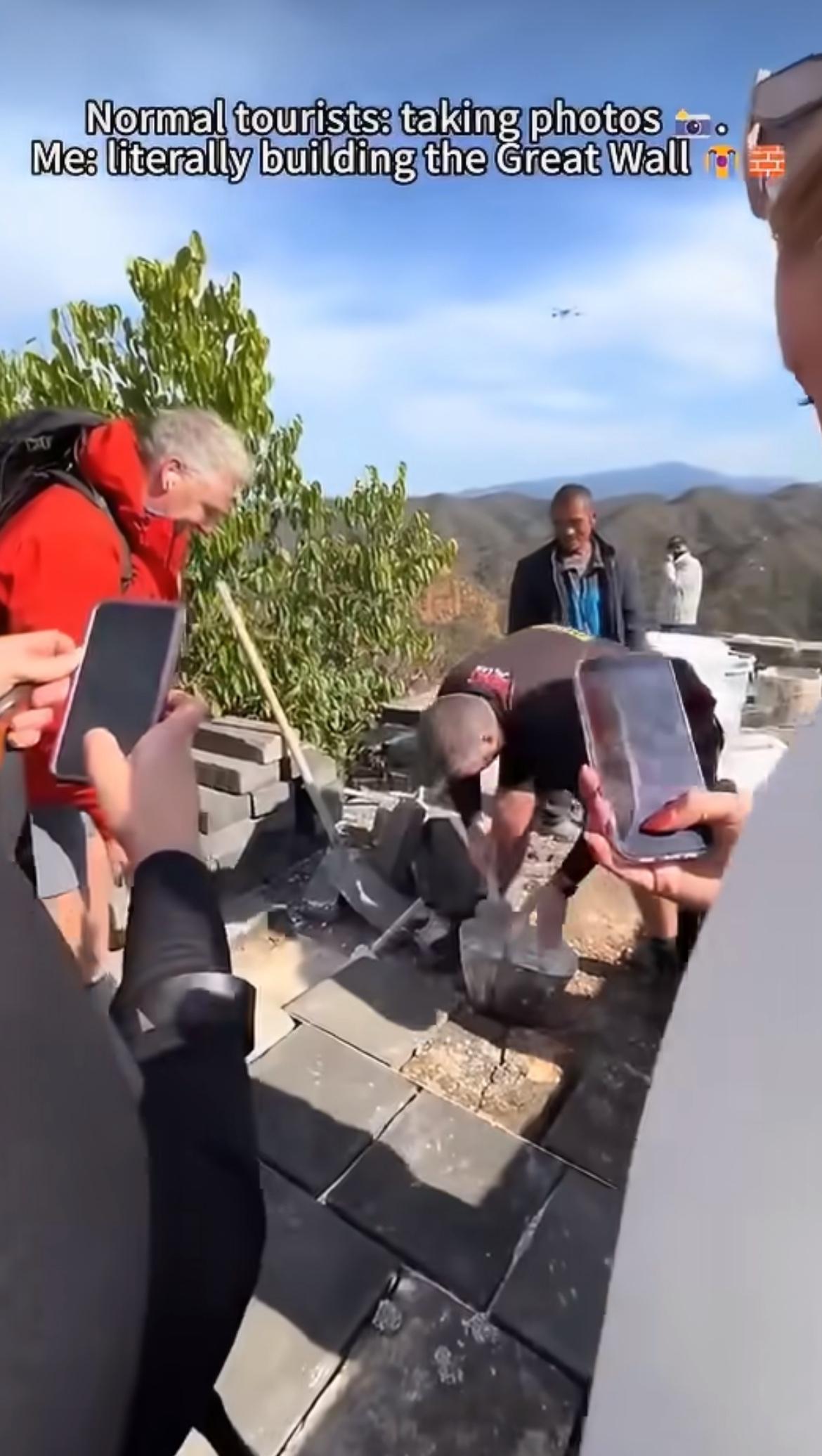 外国游客看到工人正在修复长城，而且空中还有无人机运送修复物资，几名游客纷纷加入修