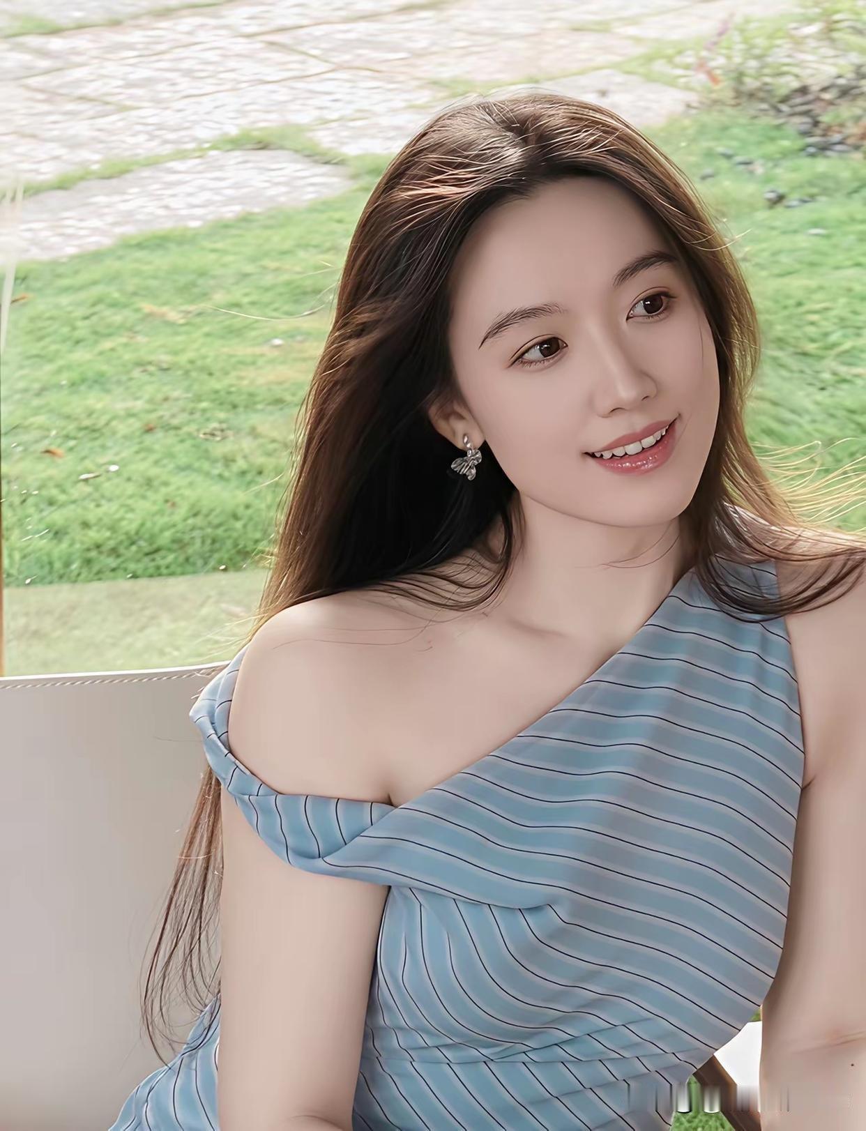 长发美女穿着条纹裙，微笑看向窗外。