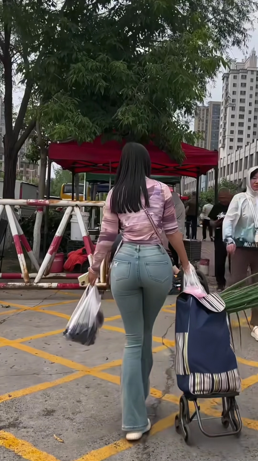 街头偶遇，她穿着时髦，粉紫上衣配喇叭牛仔裤，拖着小推车，拎着购物袋，背影都藏着对生活的热爱，平凡日常