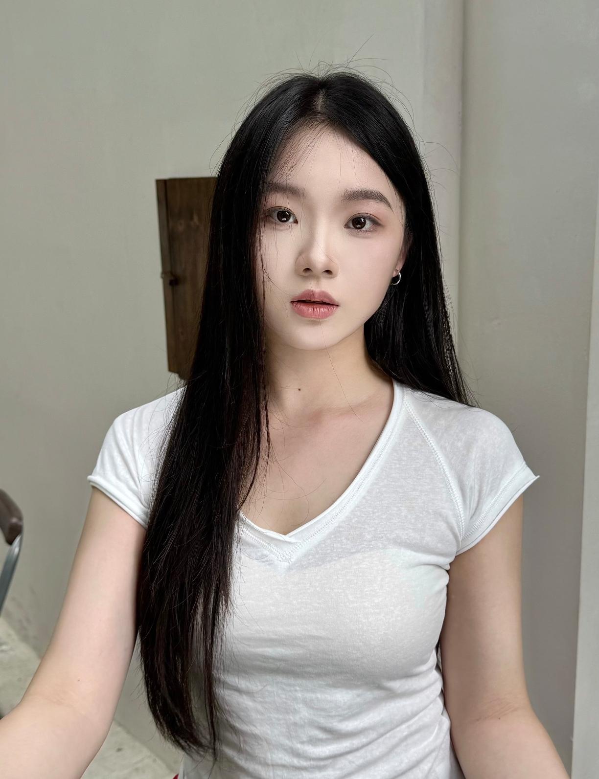 一个长发妹子穿白色T恤，看着镜头。
