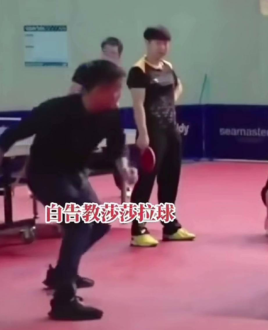 看男队主教练王皓教莎莎拉球，多认真。莎莎拿着球拍站旁边，一手叉腰，看着王皓拉球