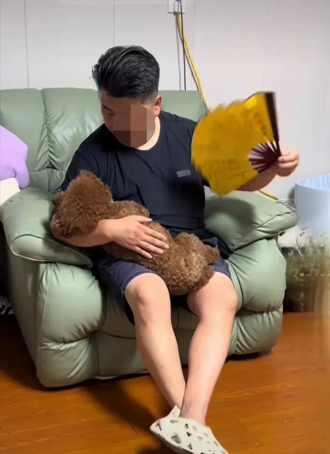 这位先生对狗狗真好，抱在怀里还给它扇着扇子，这么疼爱有加，为什么不开空调呢？二
