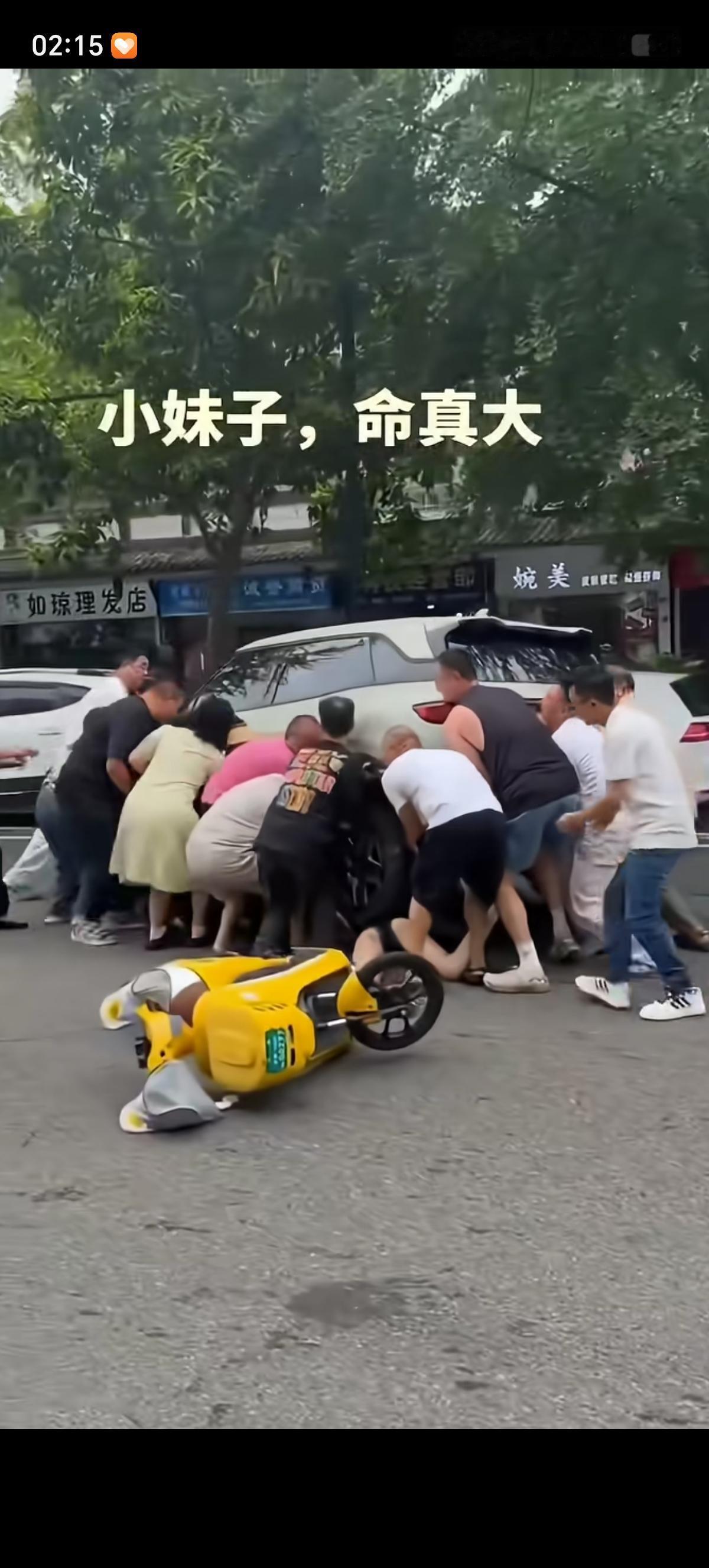 骑车电动车的少女摔出去了，正好趴着倒在地上，一辆白色轿车的车轮子凑巧压住了少女的
