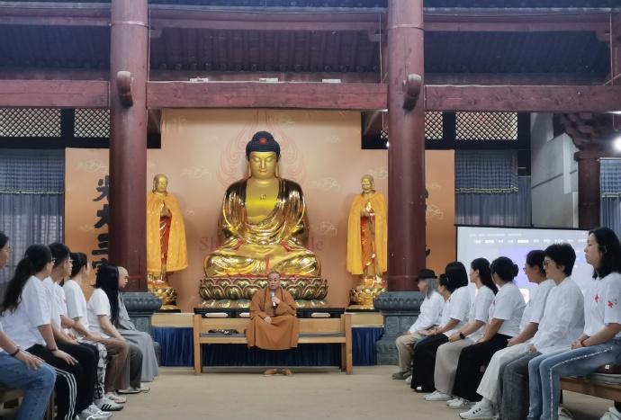 这是少林寺前方丈释永信盘腿坐在罗汉床上给下面的信众们谈佛论道。释永信身后就矗立着