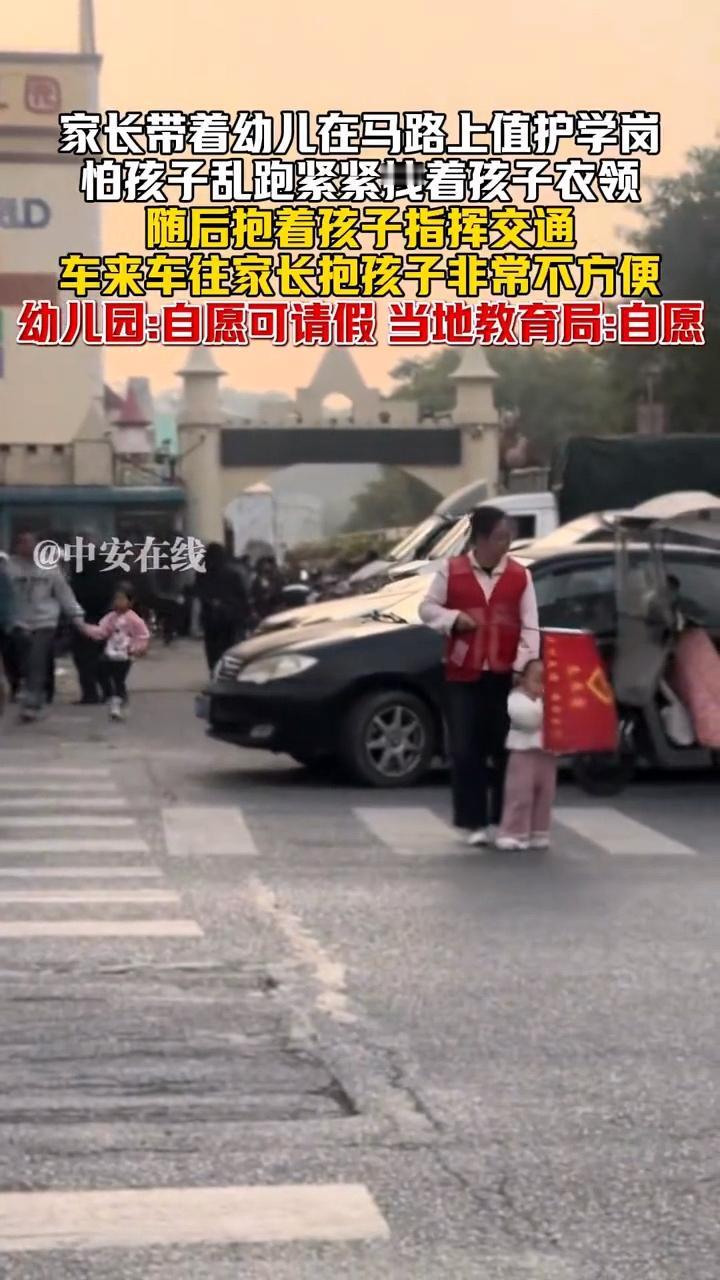 广东，一名女性家长带着还不怎么会走路的孩子，在马路上值护学岗，路上车来车往非常不