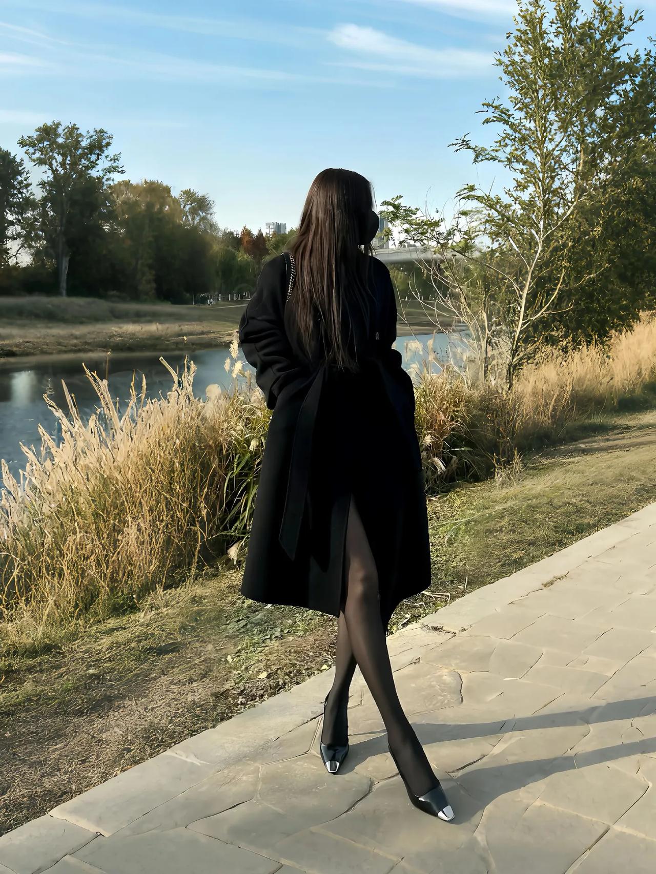 风把秋意揉进衣角，黑灰大衣裹着松弛步调。河畔草尖缀着软光，石阶上光影漫溯，林间落