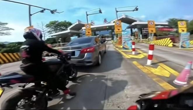 女司机在ETC通道排队时，没看后视镜就突然倒车，直接把后方摩托车的前轮给压了。