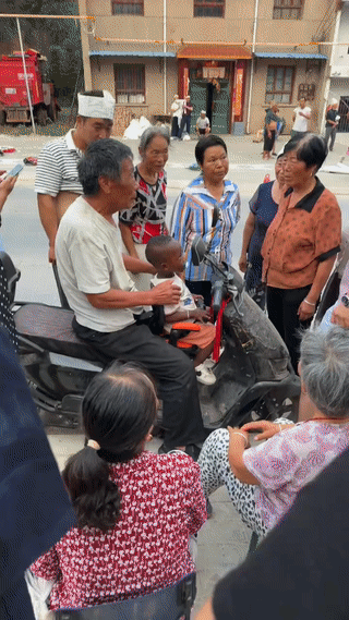 陕西一老人骑车带孩子去镇上赶集。结果他刚出现在街头瞬间就被人围观起来看热闹。
