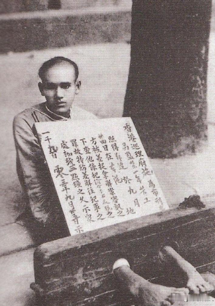 历史老照片：一名年轻男子身带枷锁，还抱了张告示。地点应该是100多年前的香港