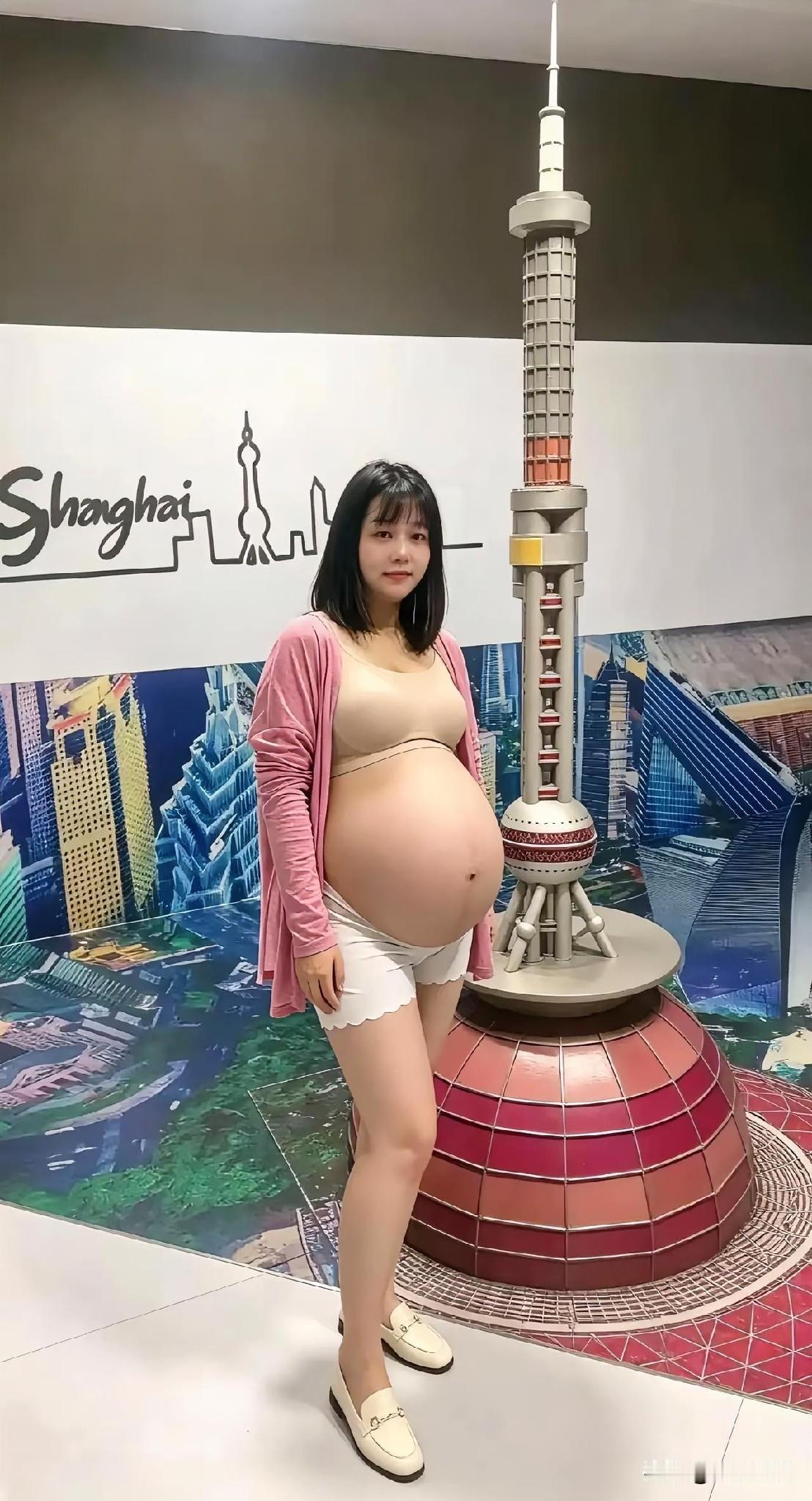 孕妇站在上海塔模型旁，微笑拍照。