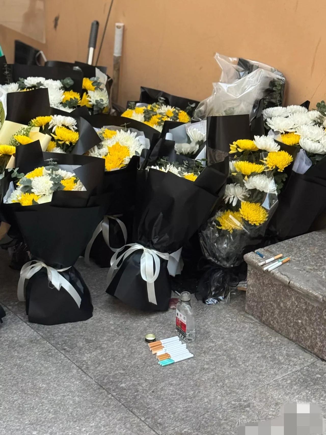 青岛大学宿管大爷被拉走后，同学们自发在门口堆满了鲜花和香烟，他养的几只流浪猫也还