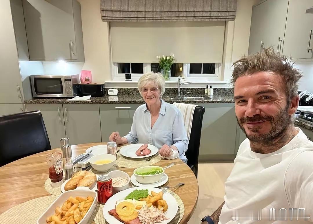 亿万富翁贝克汉姆在豪宅陪妈妈一起吃饭，桌面上有薯条，牛肉，面包，番茄酱等，有钱人