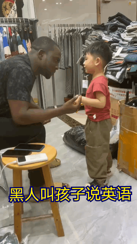 广东的一家服装店里。一名黑人男子正在教店主的孩子说英语？黑人男子教的很有耐心