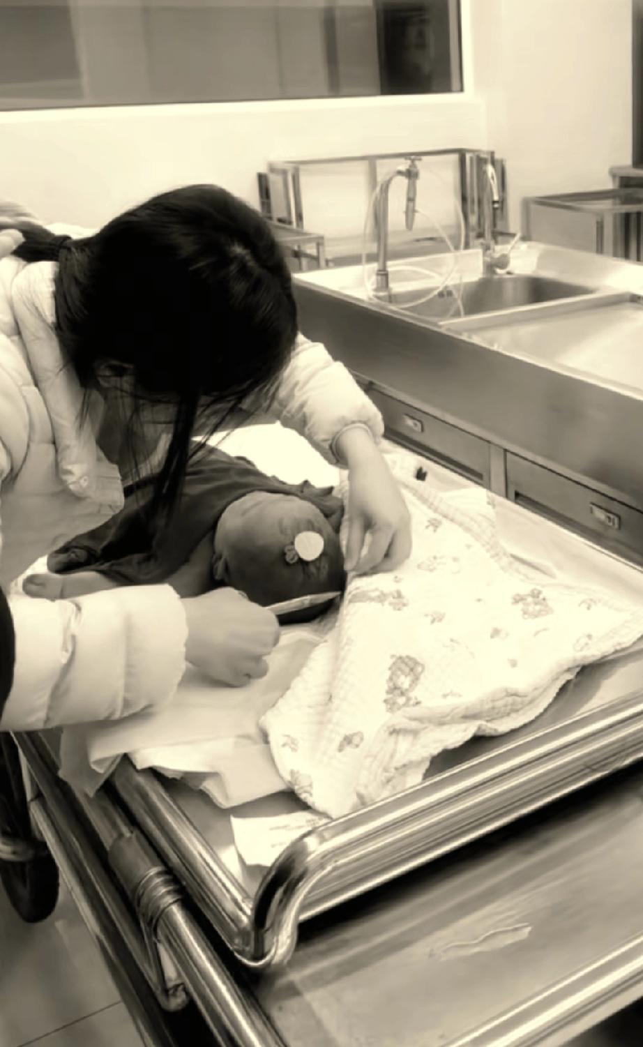 看似是在手术台上，小熙熙没有穿衣服，只是盖了个小毯子，妈妈弯着腰，小心翼翼的给宝