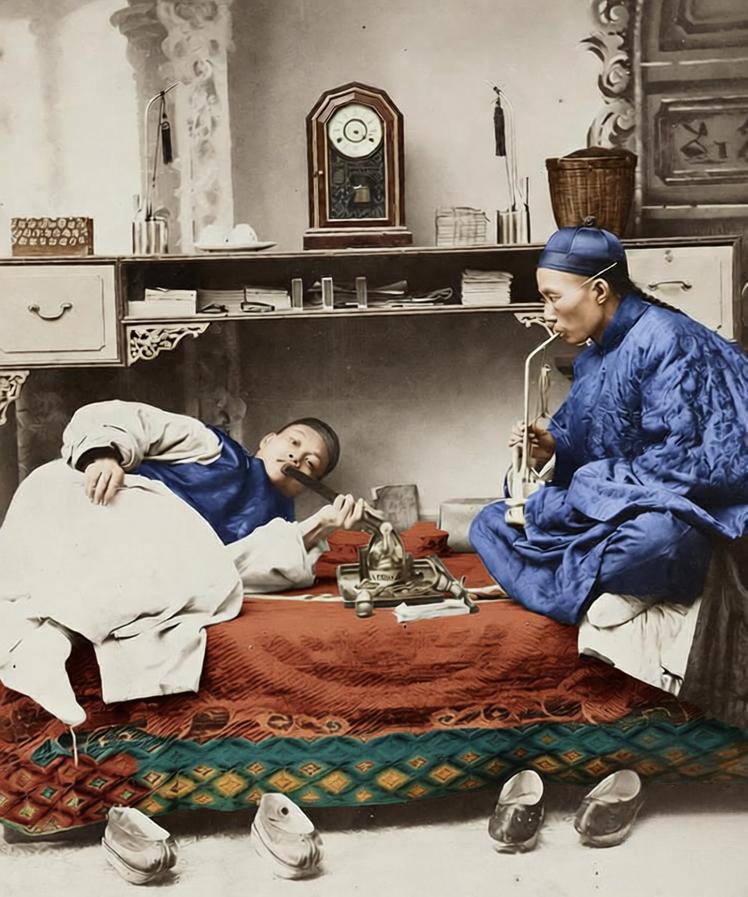 晚清，鸦片电里烟榻铺着织纹褥子，一人慵懒卧在榻上、嘴衔烟枪，另一人坐于榻边吞云吐