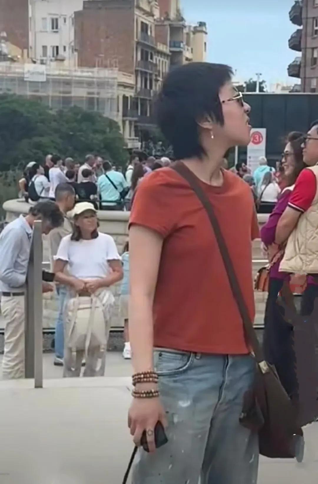 窦靖童现身西班牙街头，中性打扮的窦靖童红橙色圆领T恤衫，搭配浅蓝色牛仔裤，斜挎包