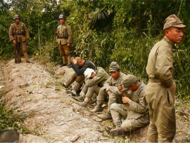 1943年常德战役后，几名战败的日本士兵或坐或蹲在泥泞的土路旁，军装破旧脏污，有