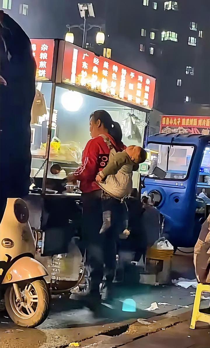 前面锅里炒的是生活，后面身上背的是希望，两岁孩子在妈妈背上睡着了，孩子的头和脚在