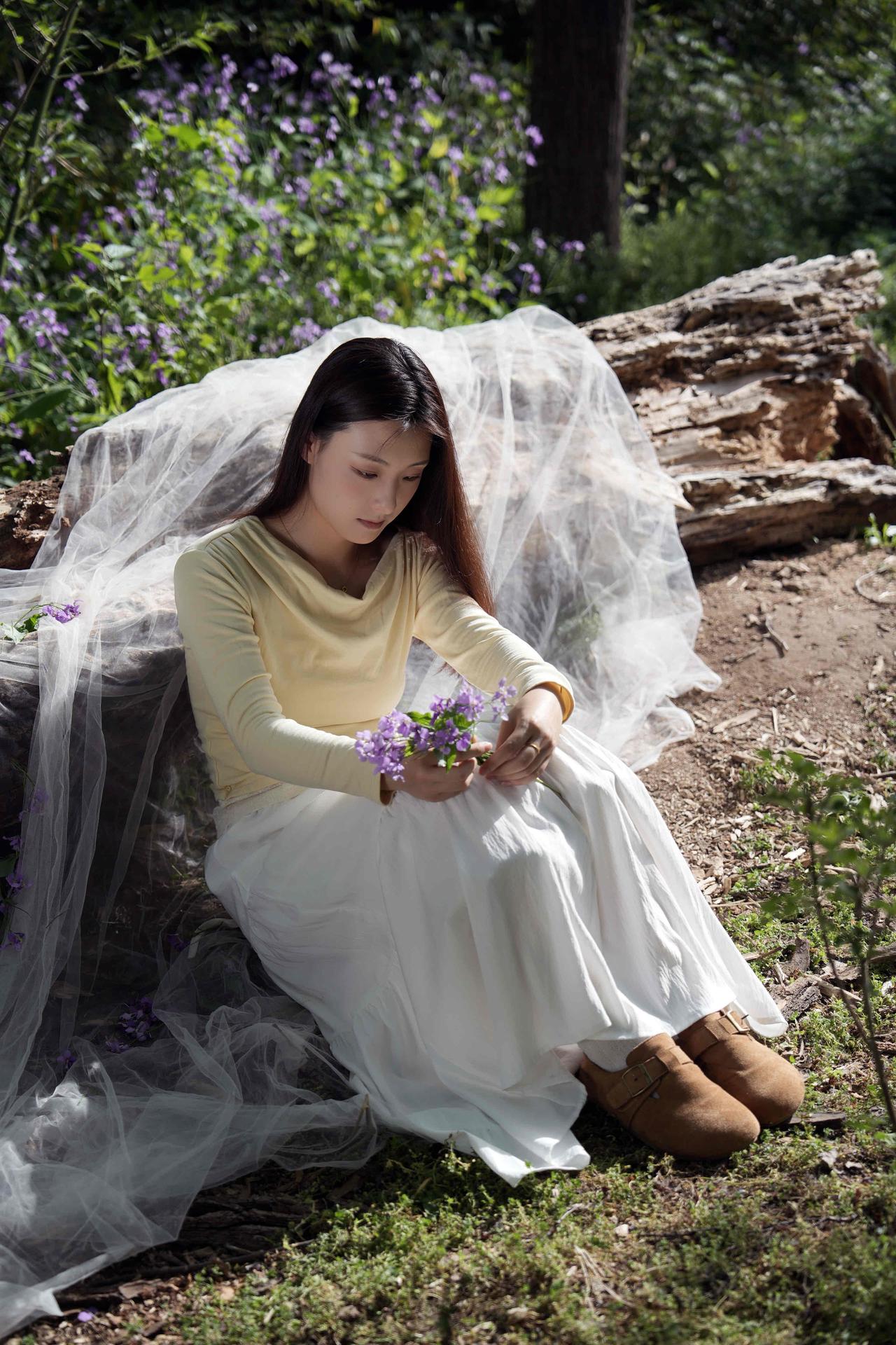 静谧森林中的梦幻少女，轻抚紫色花束，感受自然的宁静与美好。