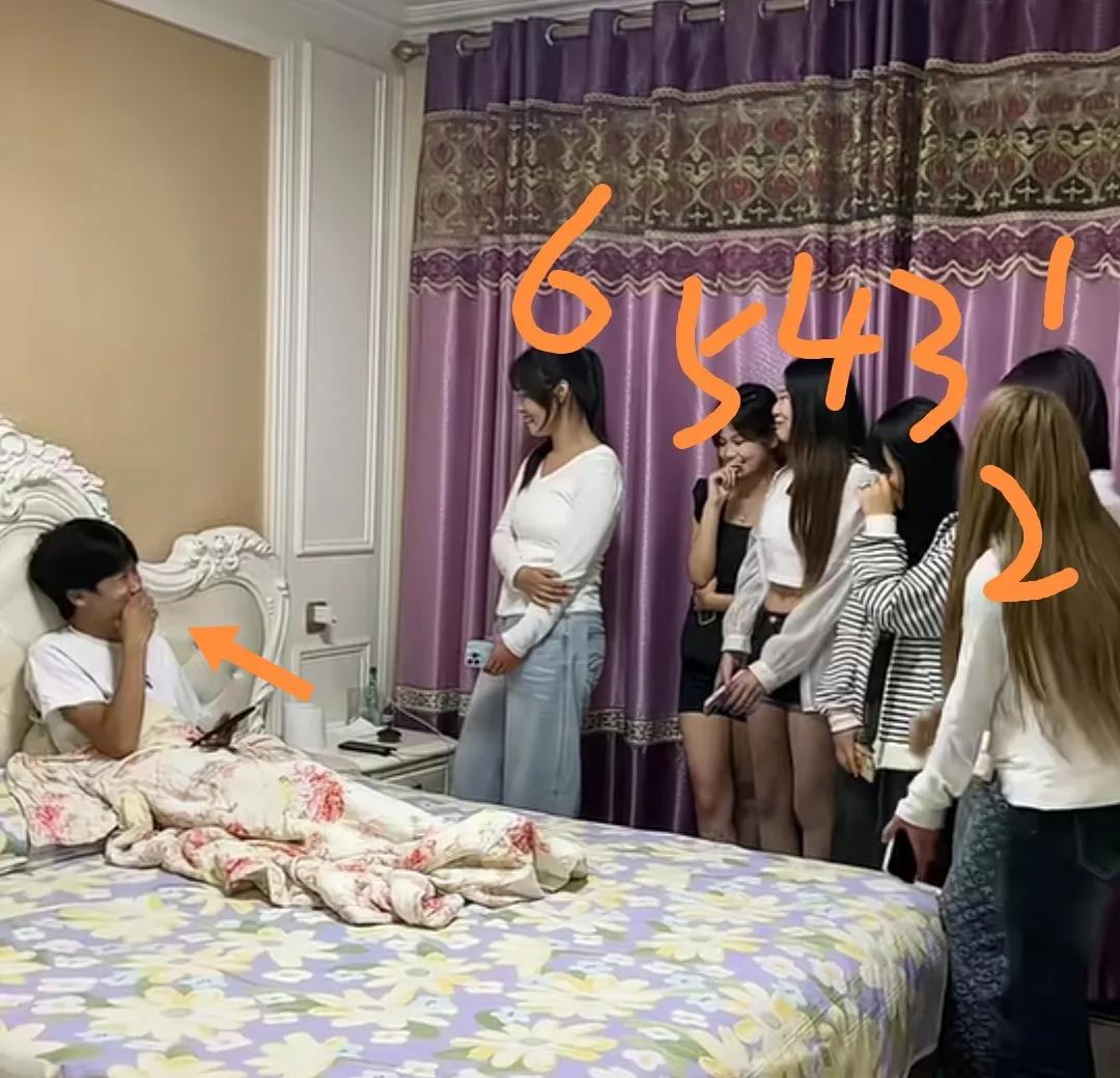 一男生脚受伤躺床上，六个女同学到家中看望他，害羞的手捂着嘴笑。