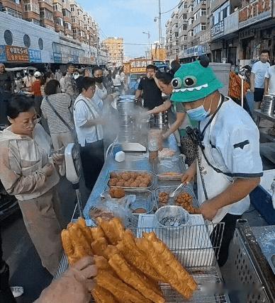 热闹的早市，一位老人直接伸手去摸摊位上的油条。摊主立刻上前阻拦，并反复提醒：入口