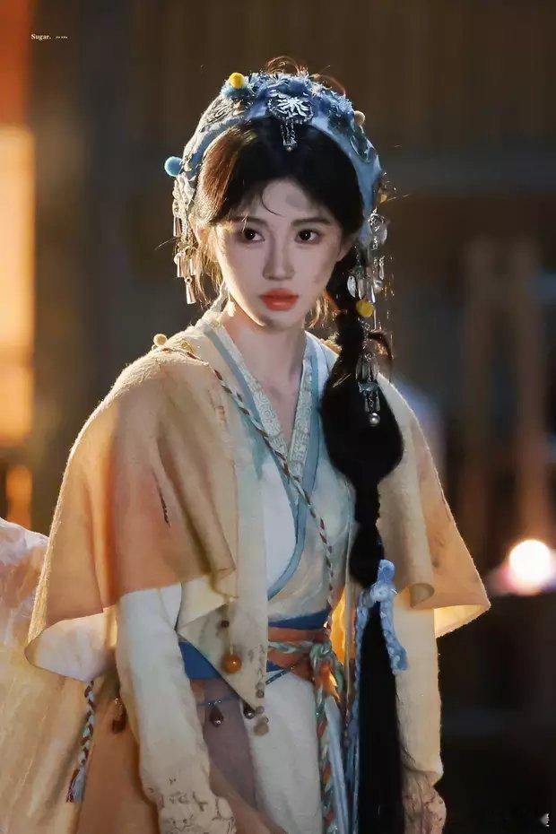 鞠婧祎拍摄《来战》路透曝光，她穿浅黄色襦裙，扎着单边辫子，头戴民族风头饰，化身脏