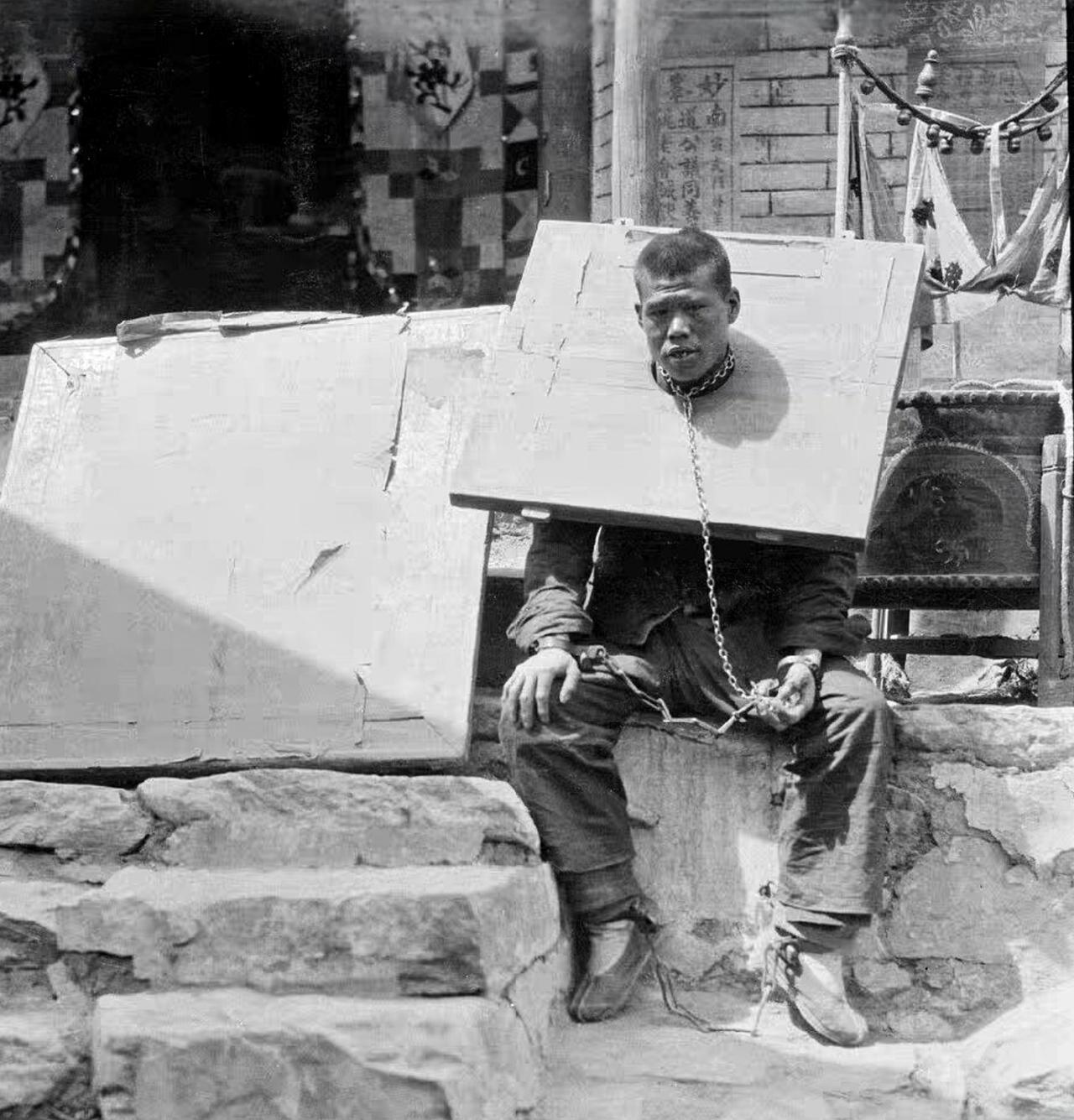 这是清末时期看押的一名囚犯，我们注意到他脖子上戴的枷锁就是一块正方形的木板，根本