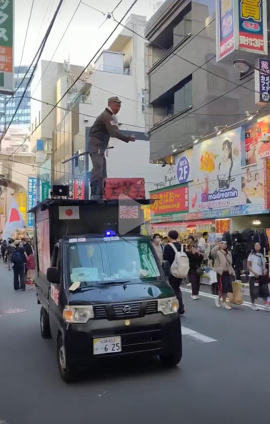 在日本的大街上，一个日本右翼分子身着二战时期的军服，手持日本军刀，站在贴着膏药旗