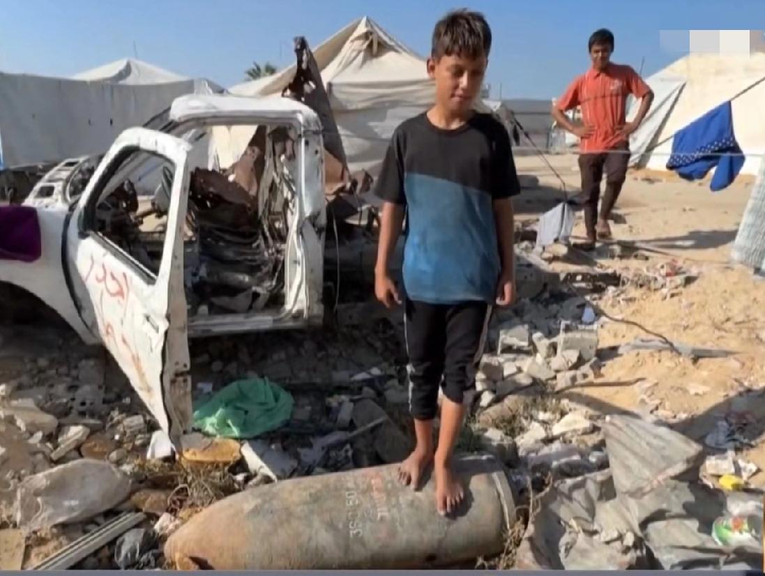 加沙的一名男孩站在一枚哑弹上面玩耍，从他的表情上看，竟然没有一丝恐慌与俱怕。以