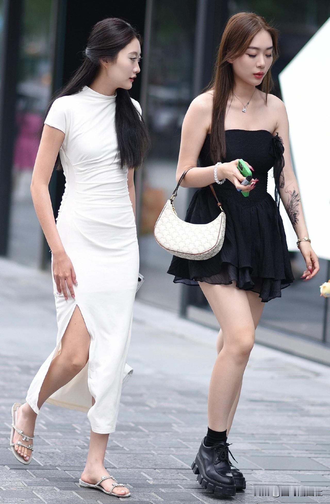 两位美女街头漫步，一个穿白裙，一个穿黑裙。