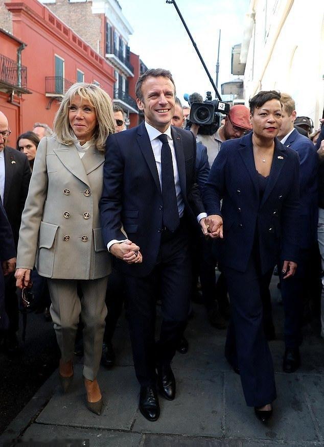 马克龙左右手牵的人都有看点，一边是他的老妻，一边是穿着女装和高跟鞋长着男人脸的人