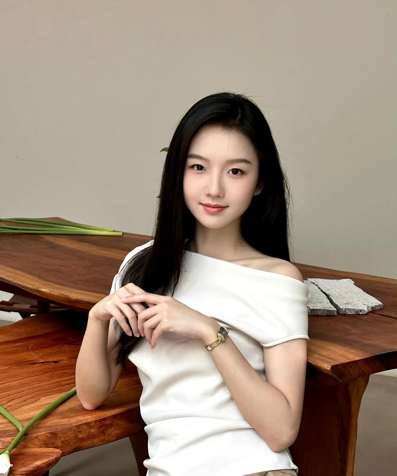 露肩白衫衬着柔荑，腕间金表漾起微光。马蹄莲落在木桌，青藤漫过石沿，她把松弛写进眉