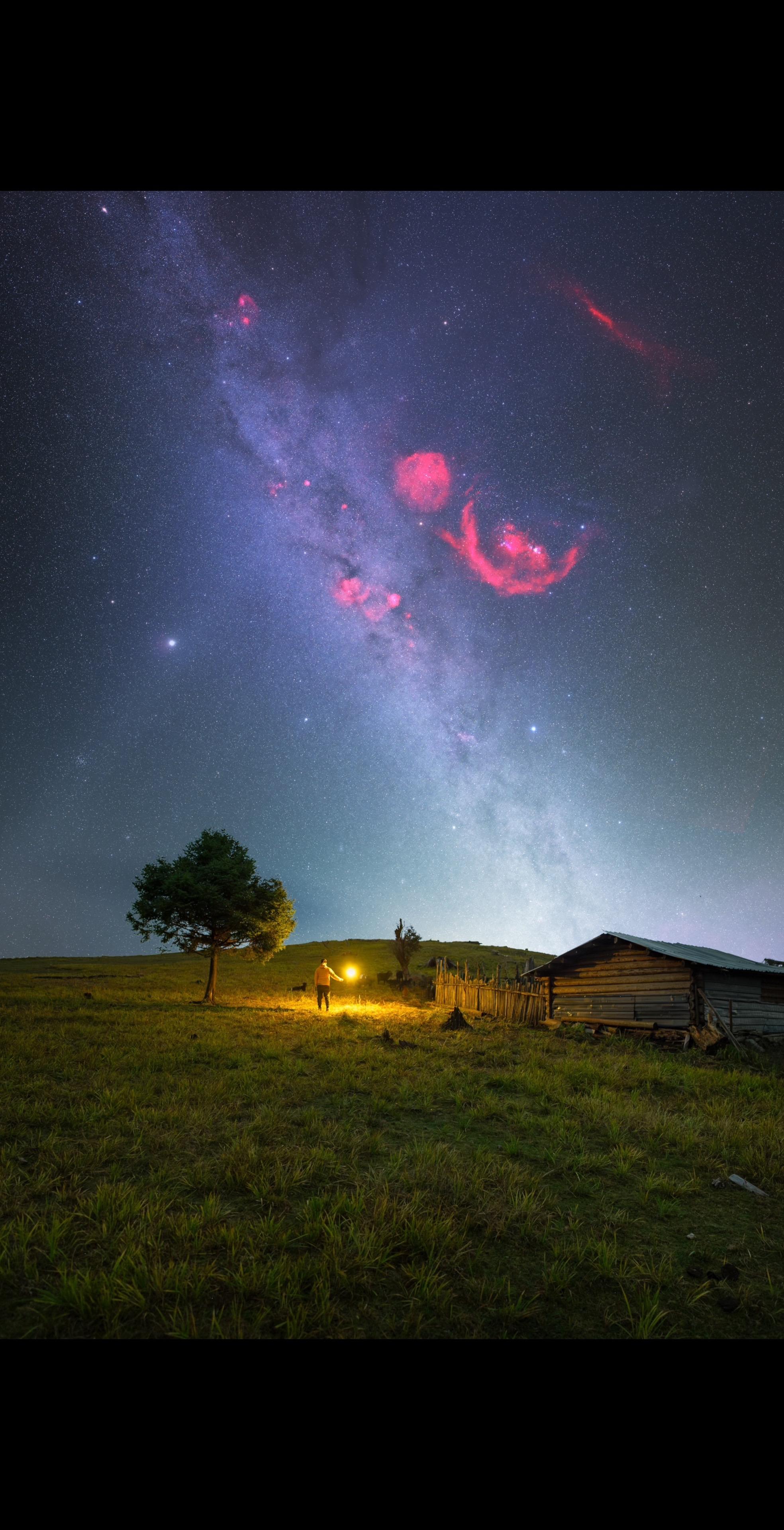 在丽江格拉丹的星空旷野之上。老旧木屋与孤树静默伫立,我手持光源,与这片...