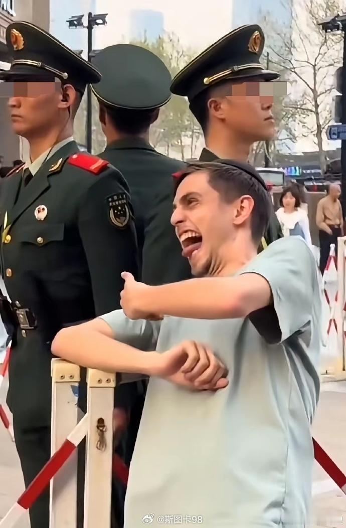 这个戴瓜皮帽的小丑在上海执勤武警旁边做鬼脸。所以说这帮小丑就是低智，我们的人民