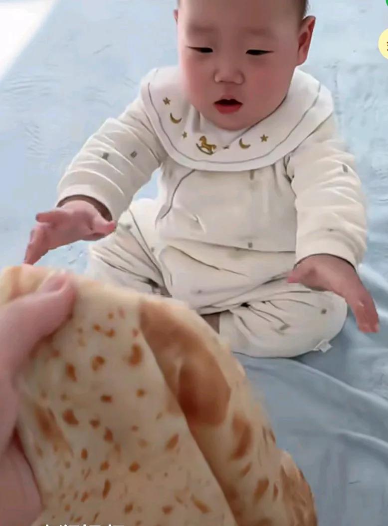 网友烙超大号饼给宝宝吃，宝宝坐在床上哭闹不止，妈妈拿着大饼走过去，宝宝接过后