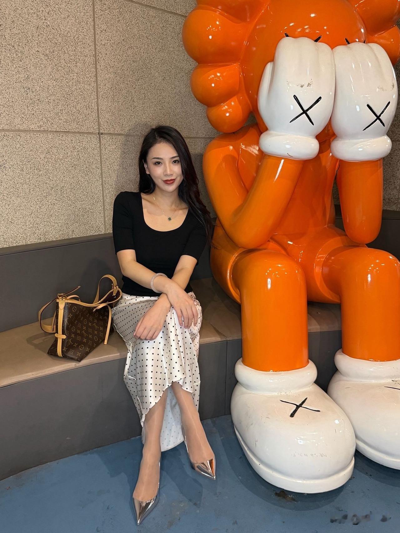 与橙色玩偶合影，黑白波点裙搭配黑色上衣，优雅又时尚！👗👠👧