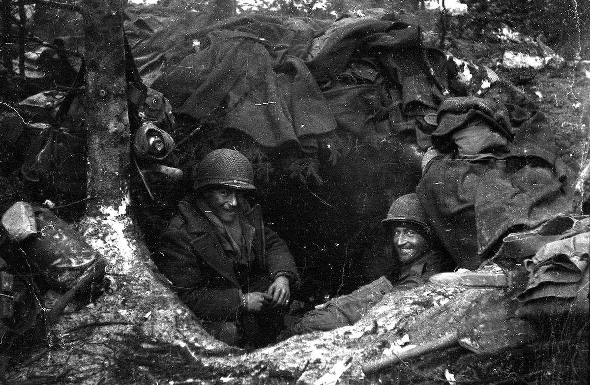 1945年，比利时境内，两名美国士兵正在一处森林隐蔽点休息。他俩的窝棚是用美军