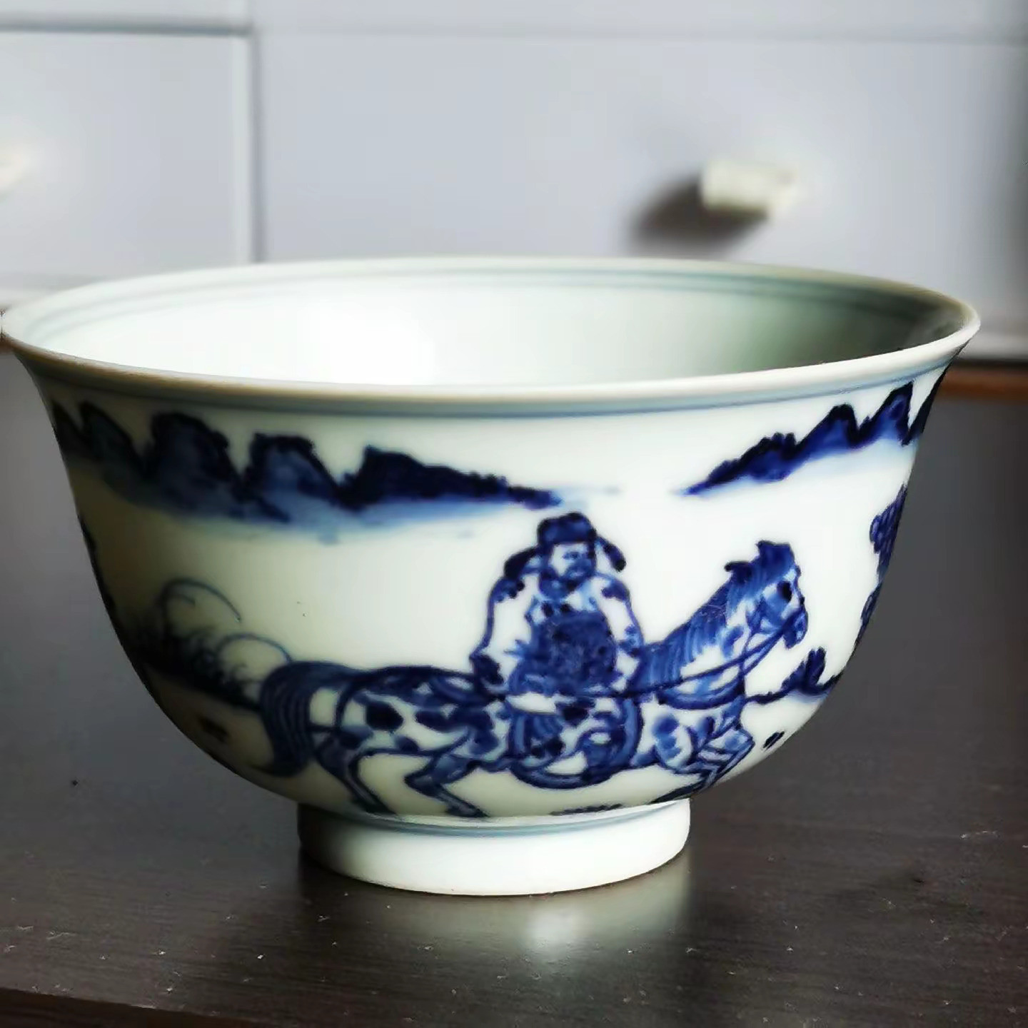 这只青花压手杯，胎质轻薄纯净，釉光细润晶莹，画工笔法流畅，画面生动有趣，人物形象