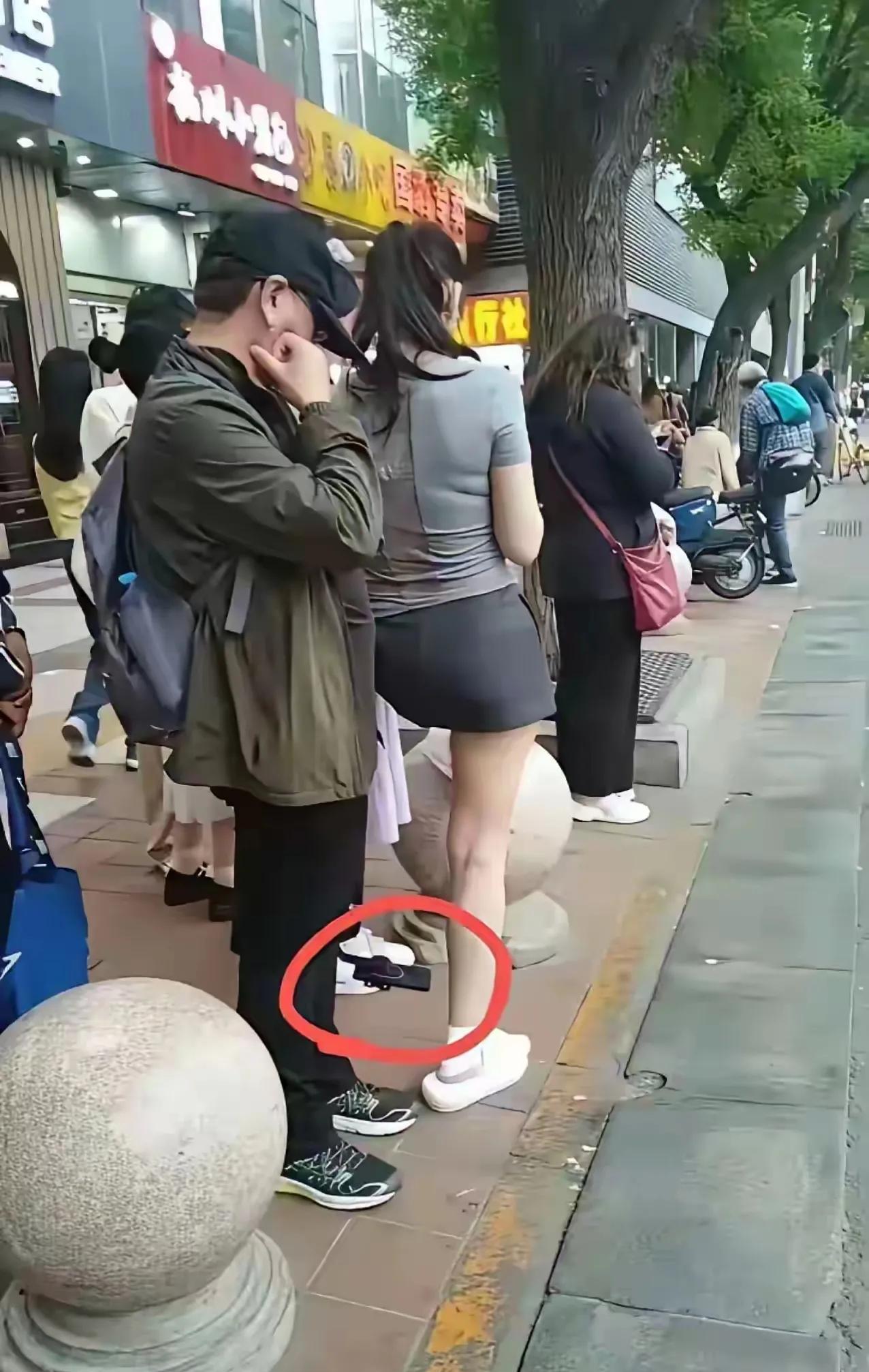 这位穿着超短裙的妇女，只顾埋头玩手机。她浑然不觉，危险正悄然逼近。一个男