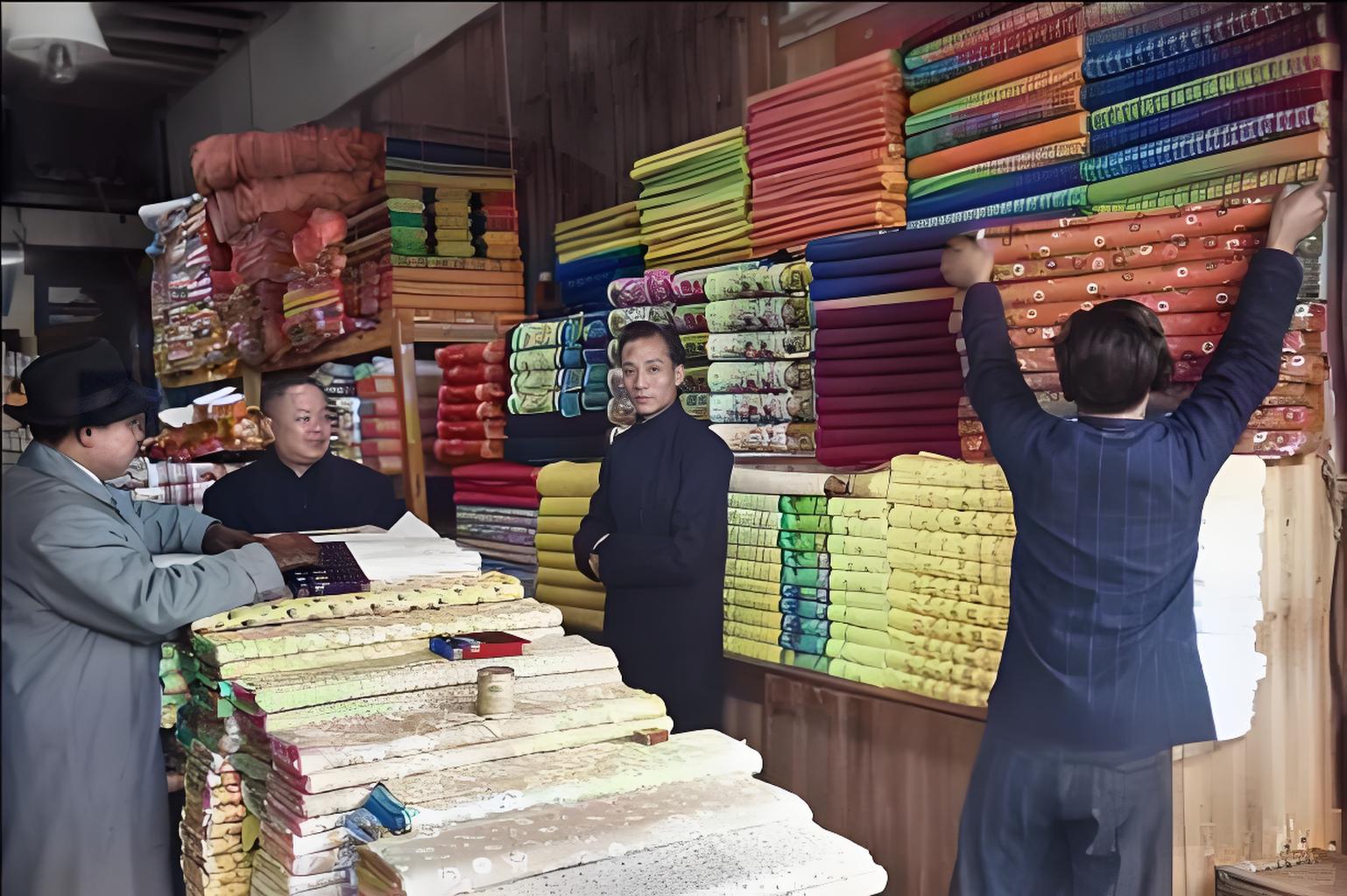 这是民国时期的布店场景。画面里，堆叠如山的布匹花色多样，店员和顾客神态各异，透着