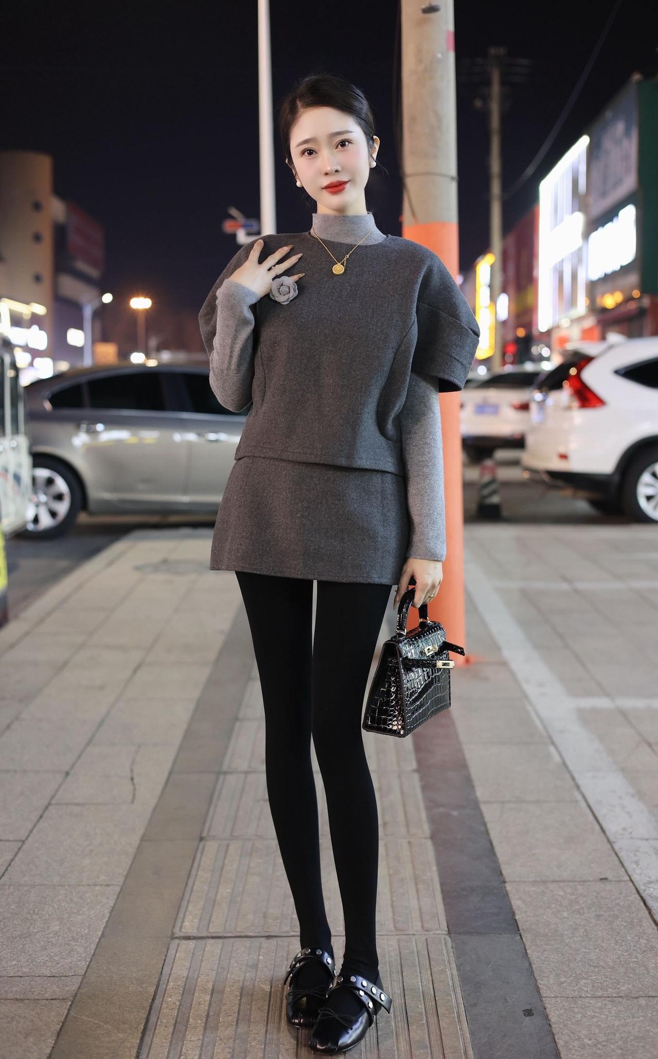 都市夜色中的优雅穿搭，灰色毛衣搭配黑色紧身裤，手拿黑色小包，尽显时尚感。
