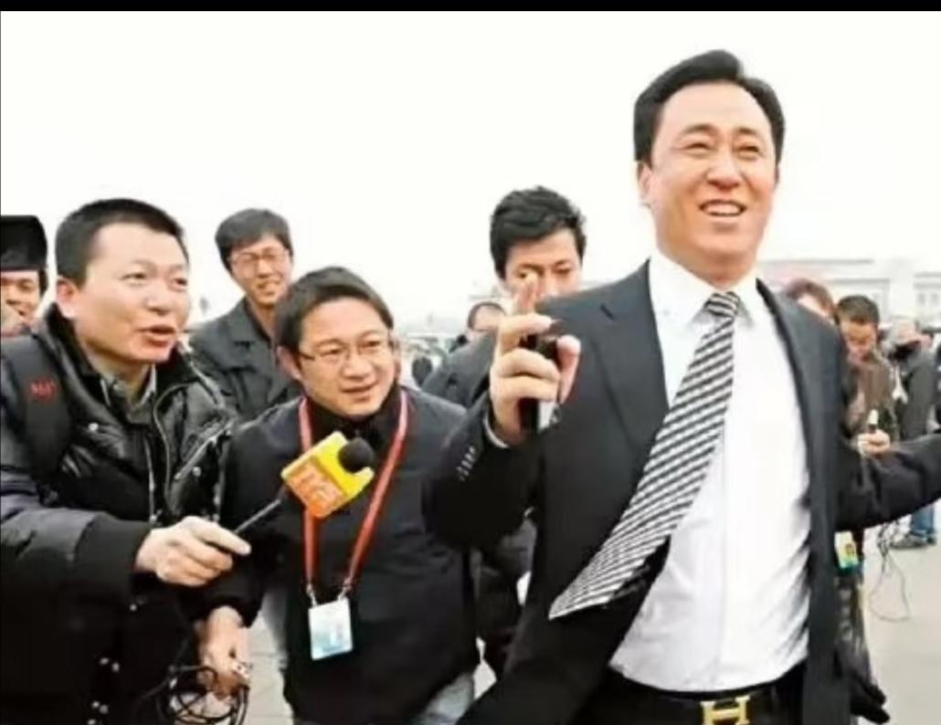 图一是许家印2012年53岁开完全国两会后被记者追着采访拍下的照片，当时的他西装
