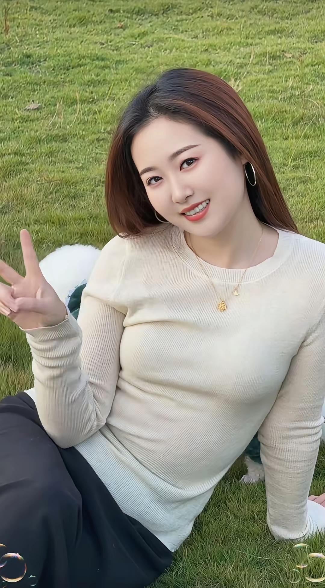 女孩在草地上比出V字手势，笑容灿烂。手型比心