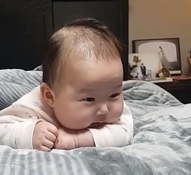 五个月宝宝趴在床上, 被爸爸逗得直吐小舌头, 呆萌的神态太可爱啦