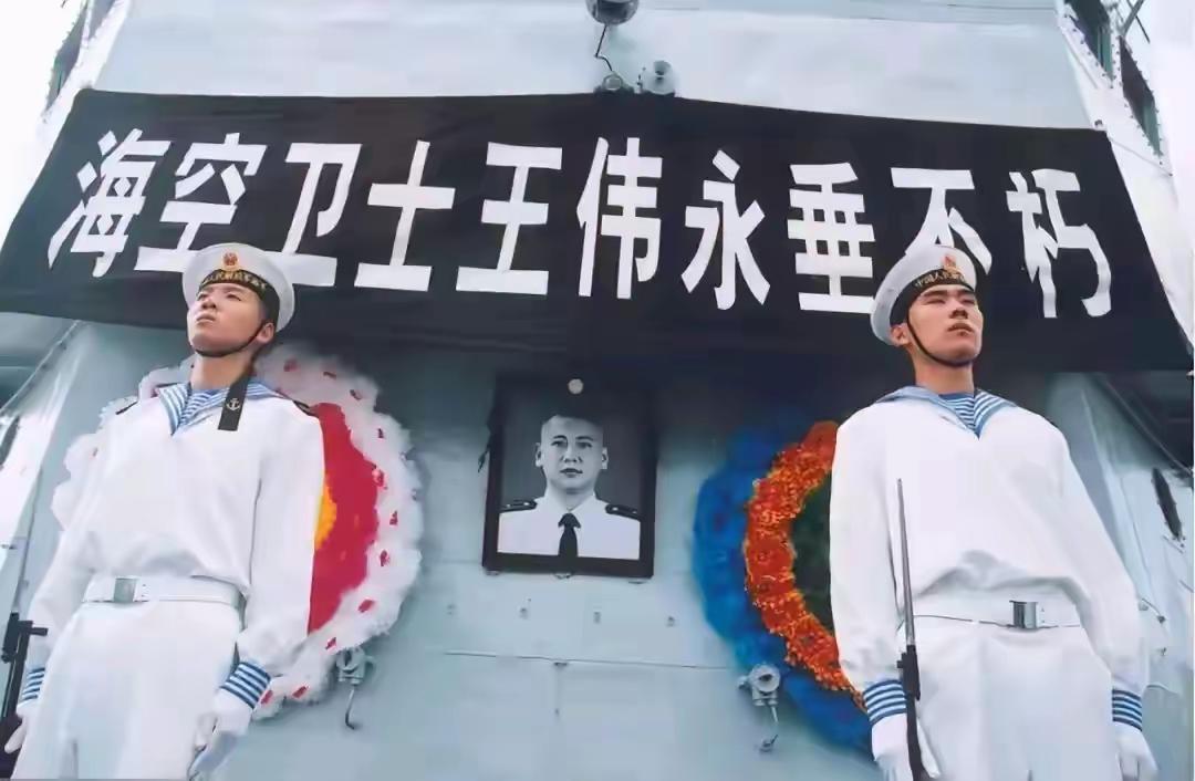 海空卫士王伟烈士：舰艇舱壁悬挂巨型黑色横幅，白字书写：海空卫士王伟永垂不朽；横幅