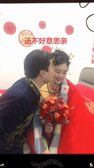婚礼现场。新郎在众人的起哄下亲吻旁边的新娘。而新娘则看起来还有点小害羞？毕